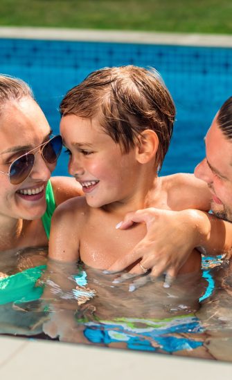 Happy parents holding their smiling son while swimming in the pool