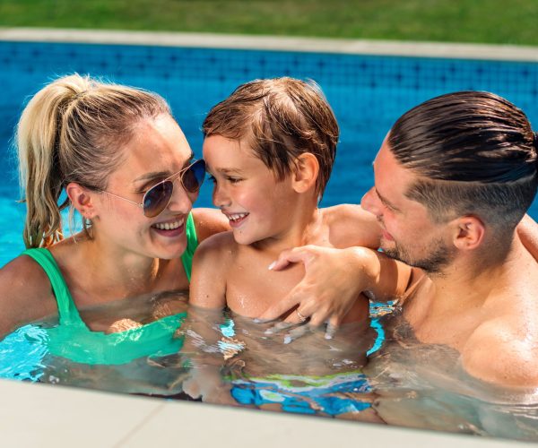 Happy parents holding their smiling son while swimming in the pool