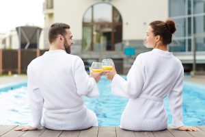 Idyllic couple toasting with glasses of juice while sitting by swimming-pool