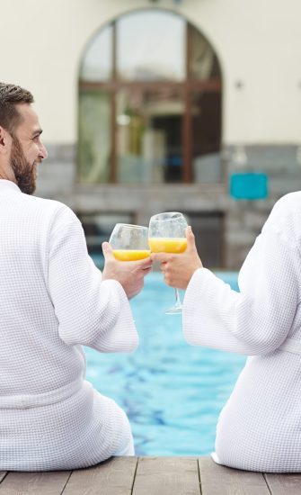 Idyllic couple toasting with glasses of juice while sitting by swimming-pool
